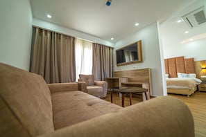 A hotel room with a sofa, armchair, a small table, a TV mounted on the wall, and a bed with a headboard. - Rais El Marsa (Algiers)