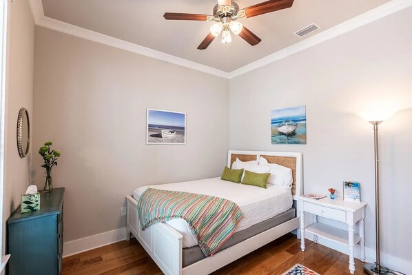 Ein Schlafzimmer mit einem Bett, einem Deckenventilator, einem Nachttisch, einer Lampe und zwei gerahmten Bildern an der Wand.