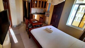 A compact hotel room with a bed, a desk, a chair, a television, and a kitchenette. - Waiyaki way Heights (Mombasa)