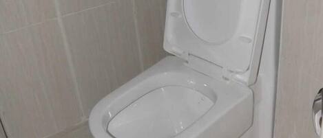 A standard white toilet in a bathroom with light-colored tiled walls and floor.