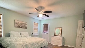 Une chambre à coucher avec un lit, une commode, un ventilateur de plafond, une porte et une fenêtre.