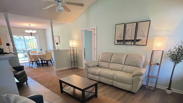 Un salon comprenant un canapé, une table basse, un fauteuil bleu, une lampe sur pied et un ventilateur de plafond.