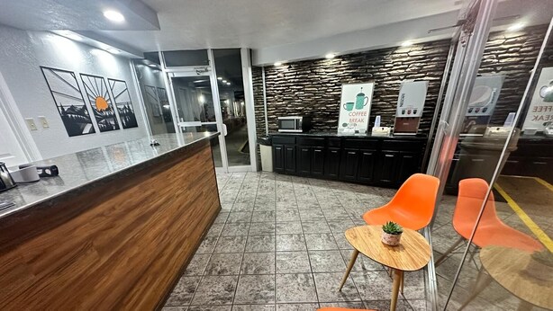 Zona de recepción con mostrador de madera, sillas naranjas, una mesa pequeña con una planta y una máquina de café.