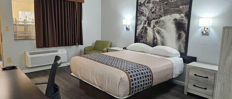 A hotel room with a bed, a desk, a chair, a heater, and a wall-mounted picture.