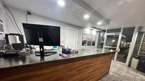 Un mostrador de recepción con computadora, teclado y monitor. Se ve una puerta y una ventana con vista al exterior.