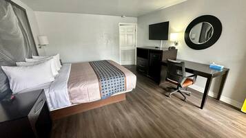 Una habitación de hotel con cama, escritorio, silla, televisor y espejo.