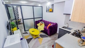 A compact living space with a purple sofa, yellow coffee table, and a kitchen area with a sink and stove. - Welcome to a spacious and cozy two bedroom @kilimani (Nairobi)