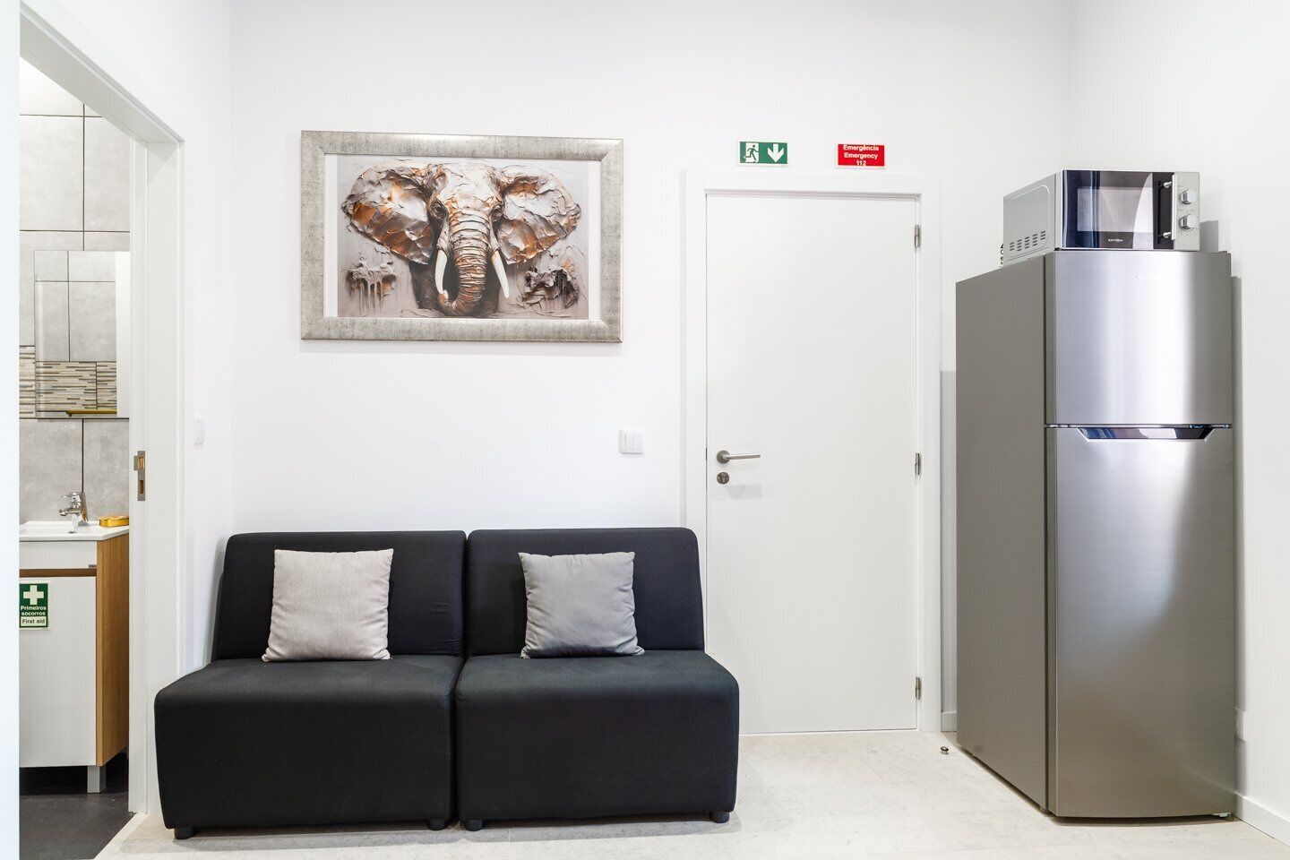 A modern hotel room with a black sofa, a stainless steel refrigerator, and a framed elephant artwork on the wall.