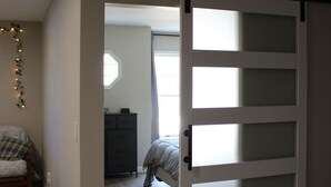 A room with a sliding door leading to another room. There is a bench and a dresser in the room. - Luxury 2-bedroom apartment in excellent Manlius with WiFi, AC (Manlius)