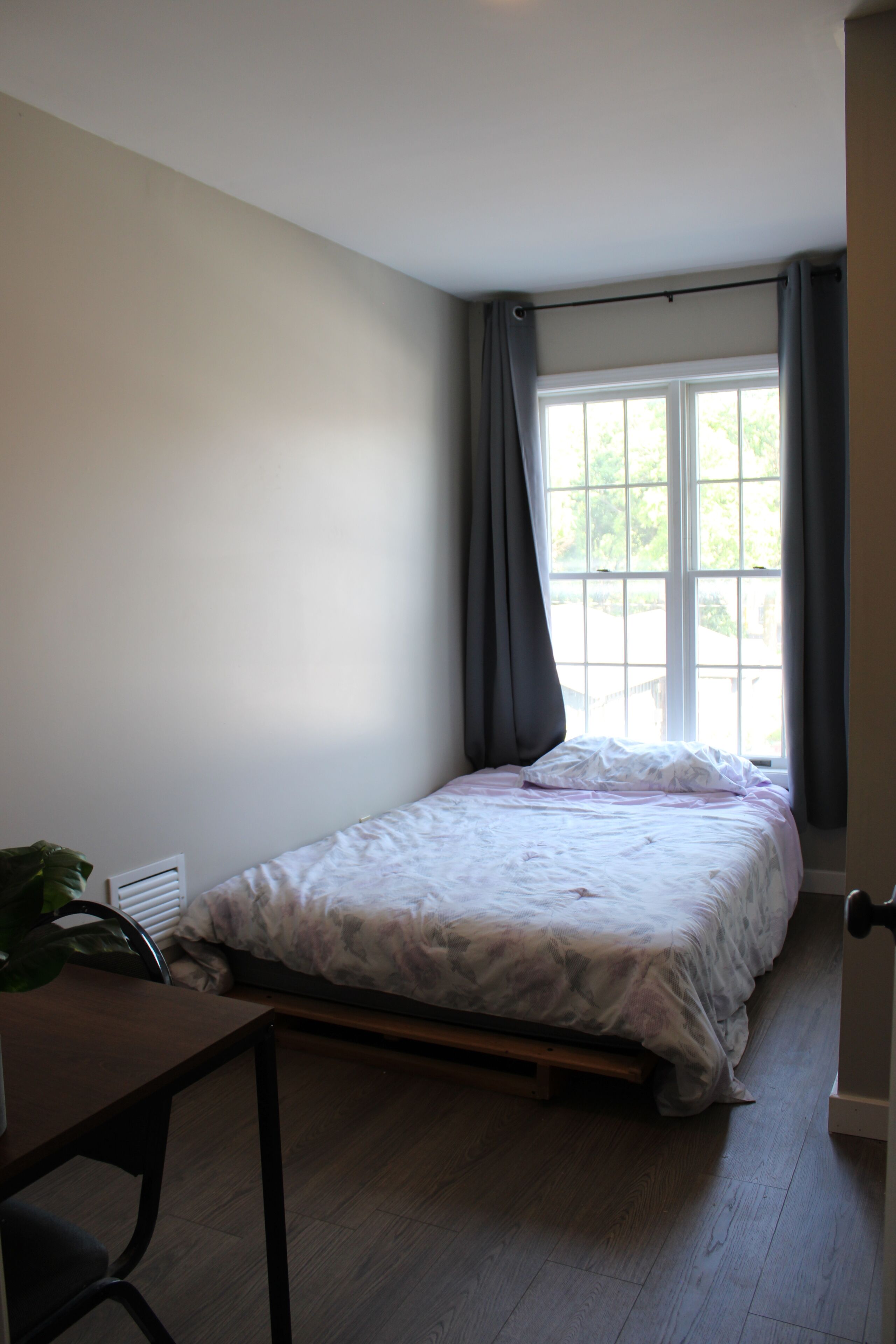 A bedroom with a single bed, a window with curtains, a radiator, and a desk with a chair.