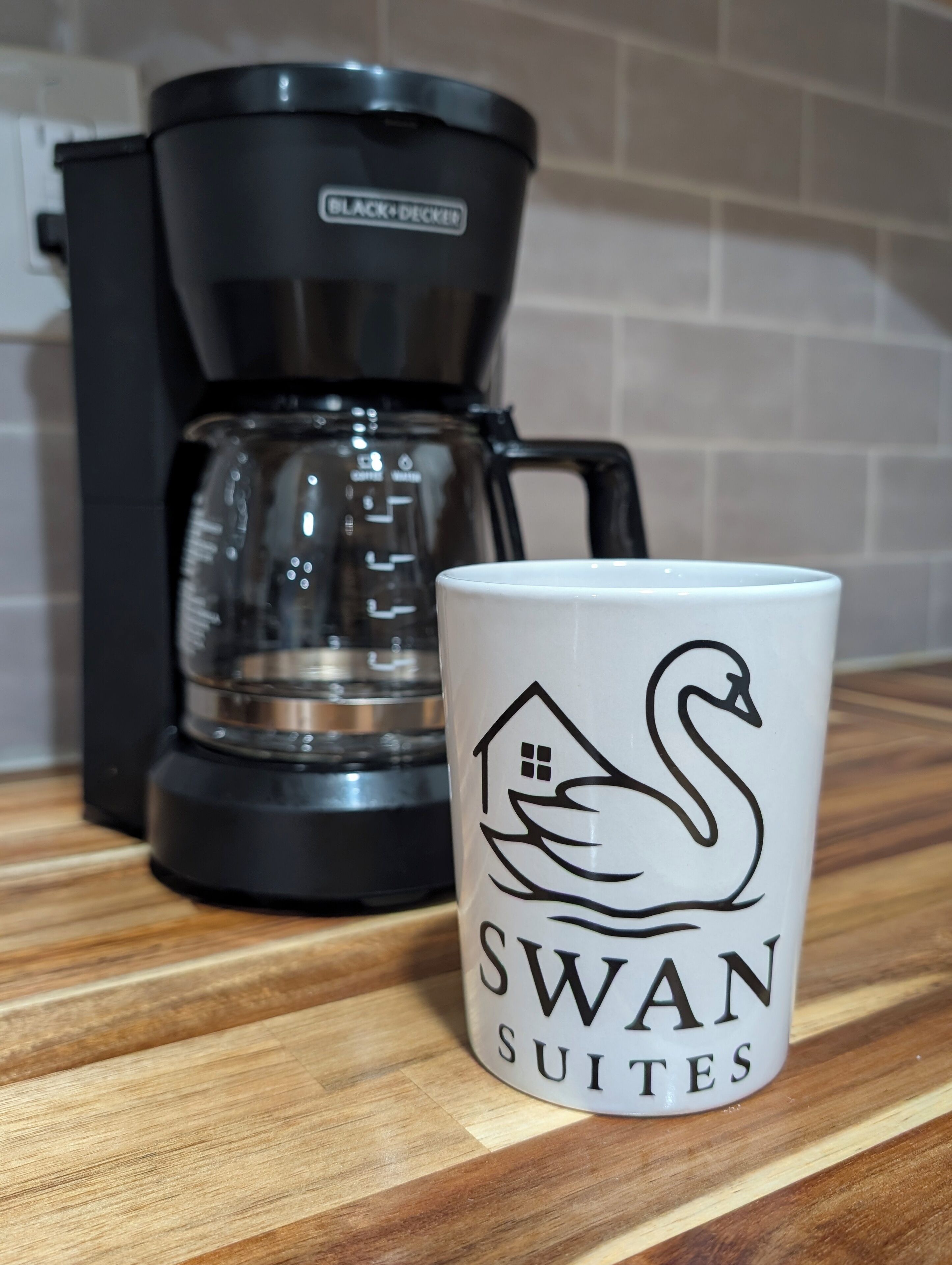 Eine Kaffeemaschine und eine Tasse mit einem Schwanenmuster auf einer Holztischplatte.