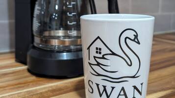 Eine Kaffeemaschine und eine Tasse mit einem Schwanenmuster auf einer Holztischplatte.