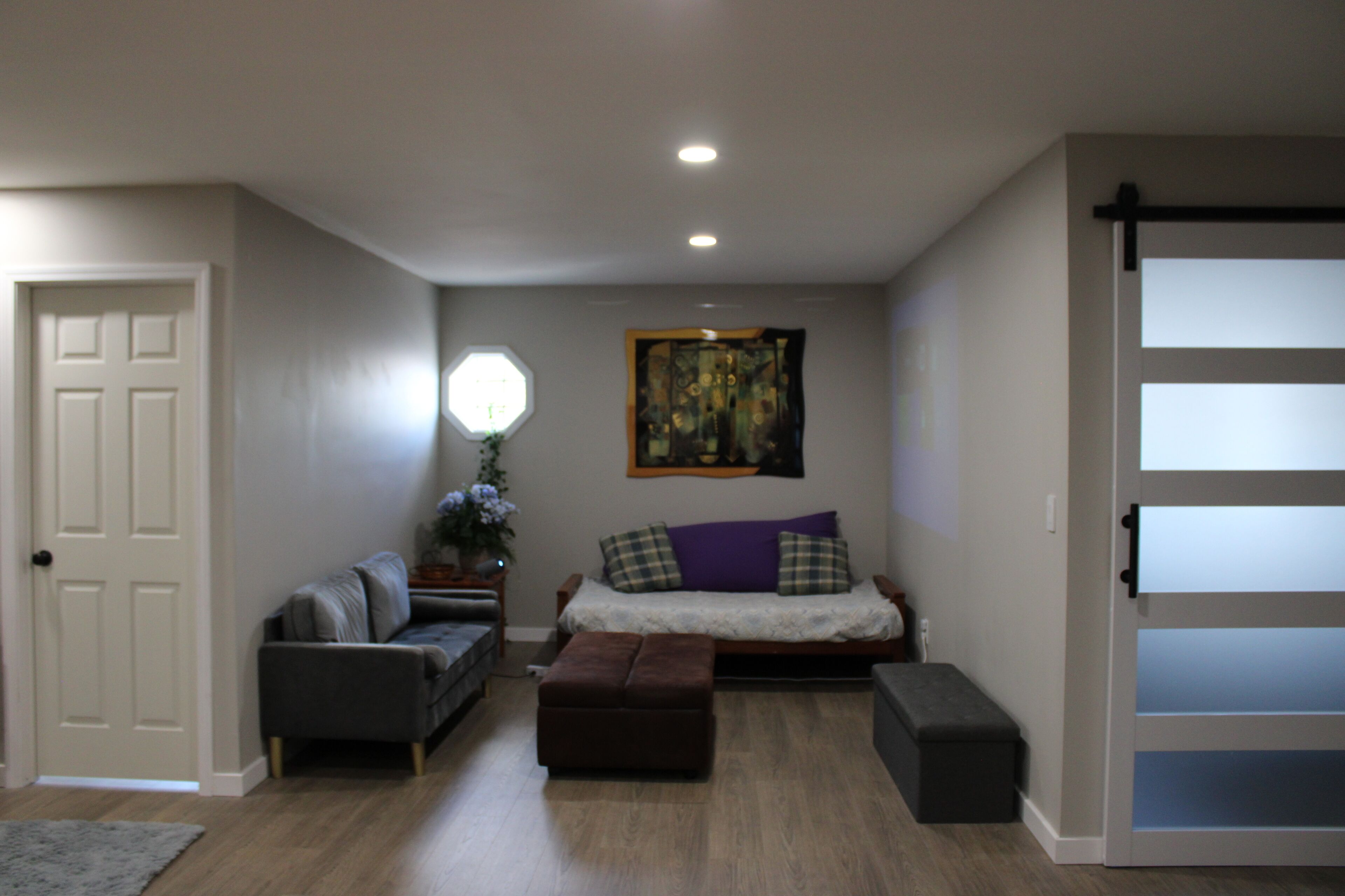 A living room with a sofa, ottoman, and a painting on the wall.