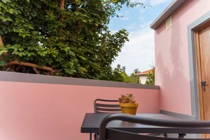 Un balcon avec une table et une chaise, une plante en pot et un mur rose.