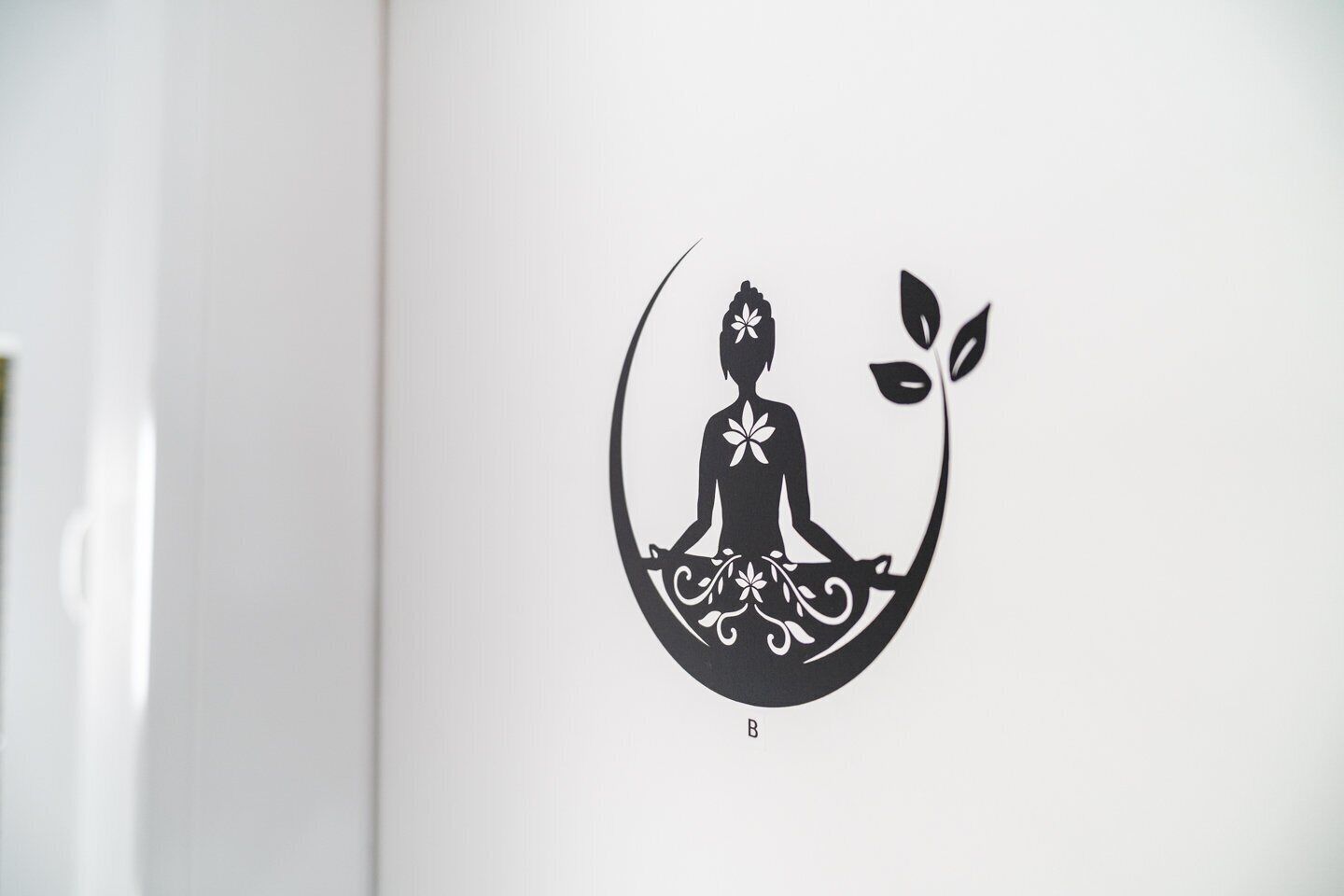 Een logo met een gestileerde figuur in een meditatieve houding, omringd door bloemmotieven.