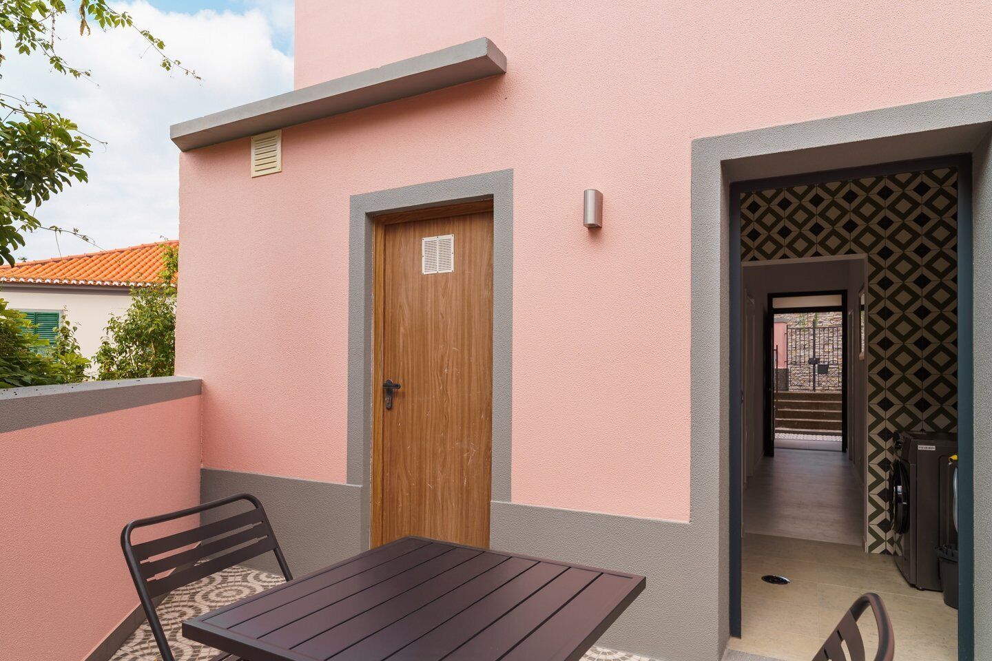 Une petite terrasse extérieure avec une table et des chaises, une porte en bois et un mur orné de motifs.