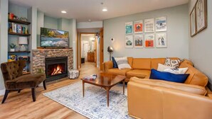 A living room with a fireplace, a sofa, a coffee table, and a bookshelf. - GroundFloor+Pool+King Bed+HotTub+Skiing (Leavenworth)