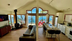 A spacious living area with a large sofa, a dining table set for four, and a kitchen with a refrigerator and stove. - Cottage with East Suite at Sahhali on the Bluffs (Pender Island)