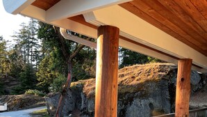 A covered outdoor deck with wooden beams and a glass railing overlooking a natural landscape with rocks and trees.