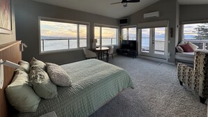 A bedroom with a bed, a desk, a TV, and a balcony with a view of the water.