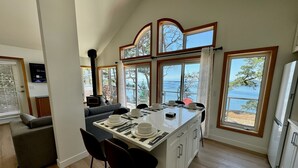 A modern kitchen with a central island, large windows with ocean views, and a cozy seating area. - Cottage w/ Vantage Suites at Sahhali on the Bluffs (Pender Island)
