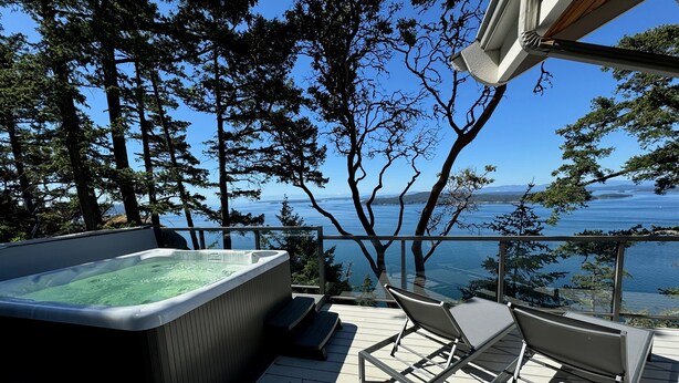 A hot tub on a wooden deck with a view of the sea and trees. - Cottage w/ Vantage Suites at Sahhali on the Bluffs (Pender Island)