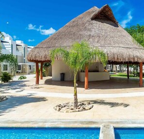 Uma construção com telhado de palha e uma piscina em primeiro plano.