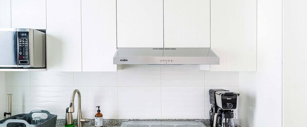 Uma cozinha moderna com armários brancos, exaustor de aço inoxidável, micro-ondas embutido, máquina de café e dispensador de sabonete no balcão.