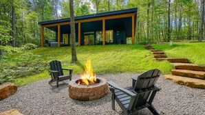 Eine moderne Holzhütte mit Feuerstelle und Sitzgelegenheit, umgeben von einem Wald.