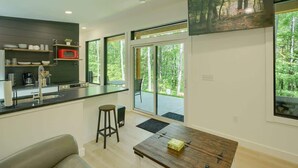 Eine moderne Küche mit integriertem Mikrowellenherd, einer Kaffeemaschine und einem Spülbecken. Große Fenster bieten einen Ausblick ins Freie.