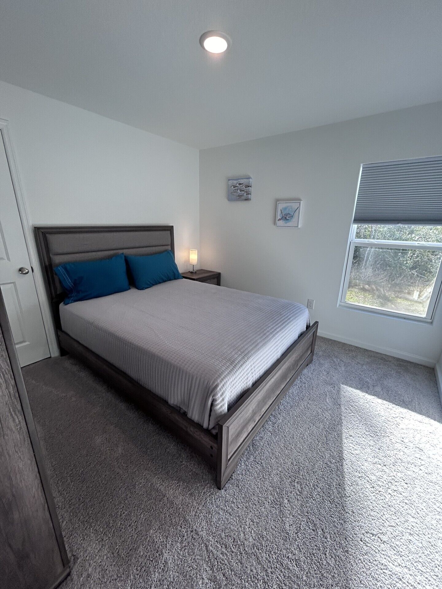 A bedroom with a bed, a nightstand, a window, and a door.