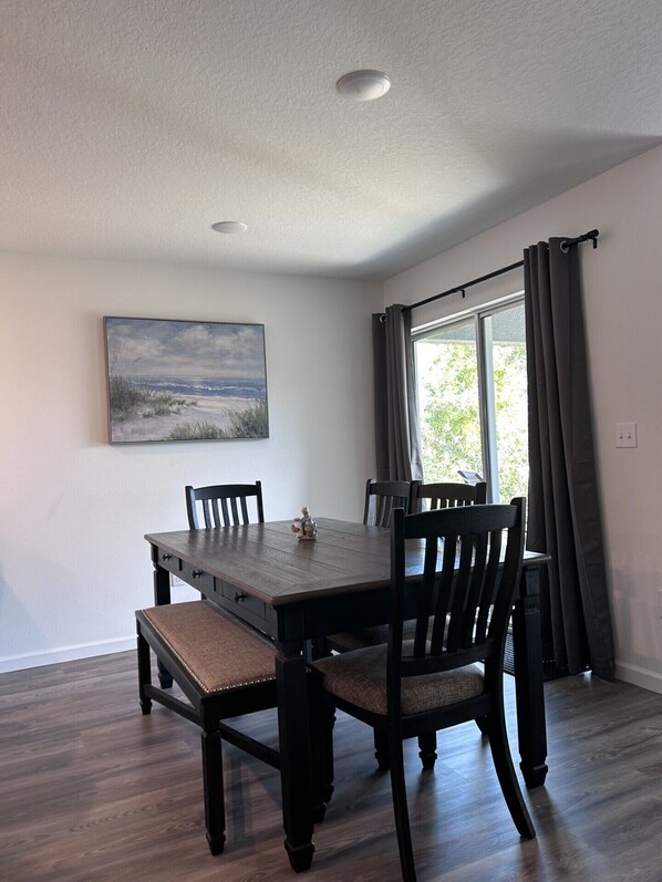 A dining room with a wooden table and chairs, a painting on the wall, and a window with curtains.