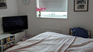 A bedroom with a bed, a TV, a window with a curtain, a clock, and a framed picture on the wall. - Quite location near to the canal (Hythe)