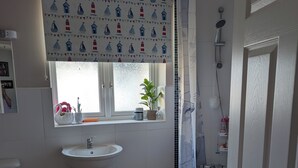 A bathroom with a white sink, a window with a nautical-themed curtain, a shower, and a wooden floor. - Quite location near to the canal (Hythe)