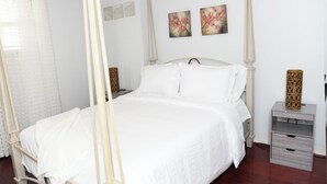Ein Schlafzimmer mit Himmelbett, weißer Bettwäsche, zwei Wandbildern und einem Nachttisch mit dekorativer Vase.