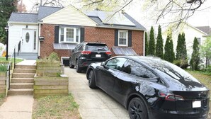 Ein Wohngrundstück mit geparkten Autos, ein Haus mit Backsteinfassade und ein kleiner Gartenbereich mit Holzstufen, die zur Haustür führen.
