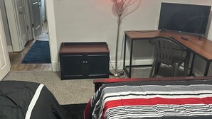 Habitación de hotel con cama, escritorio con computadora, televisor y lámpara fijada a la pared.