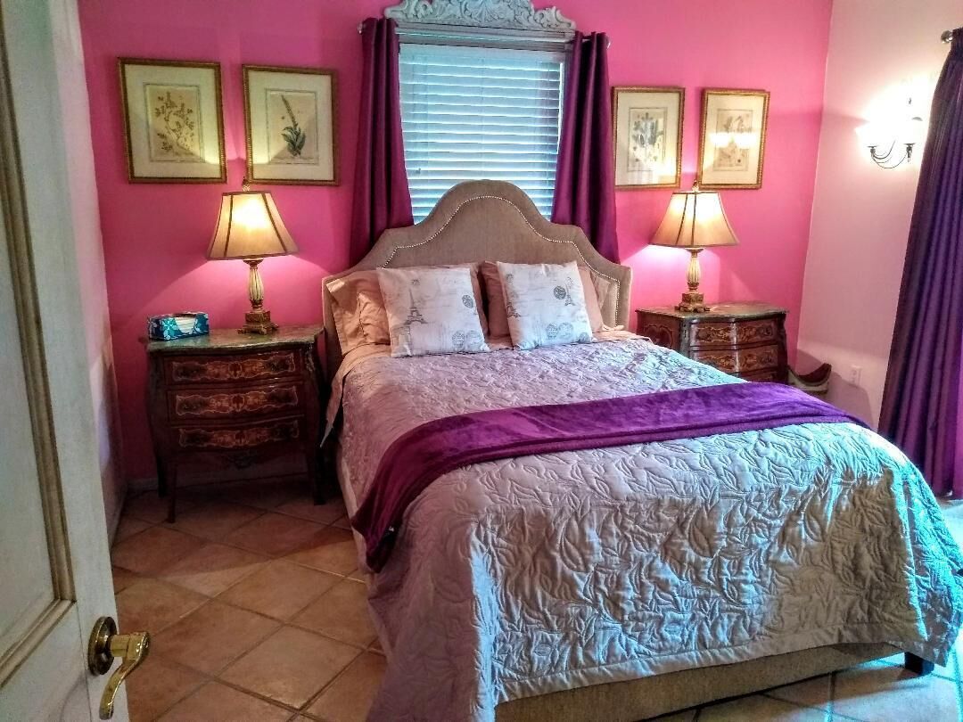 A bedroom with a bed, two bedside tables, a window with curtains, and wall-mounted lamps.