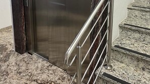 Un ascenseur doté d’un panneau indiquant qu’il est accessible aux personnes en fauteuil roulant, d’une rampe métallique et d’un escalier en marbre.