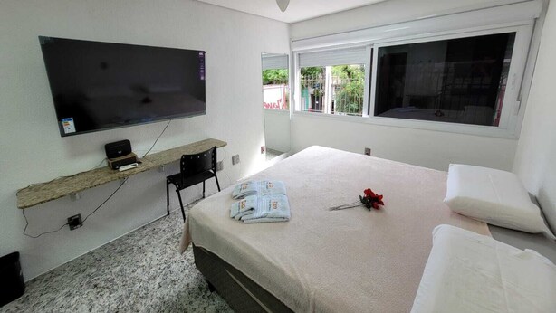 Une chambre à coucher avec un lit, un téléviseur fixé au mur, un ventilateur de plafond et une fenêtre donnant sur un paysage verdoyant.