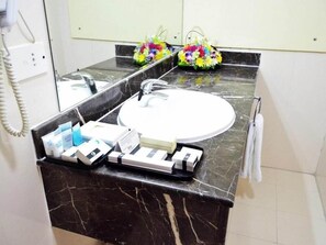 A bathroom with a marble countertop, a white sink, and a mirror. There are toiletries on the counter, and a telephone is mounted on the wall. - Palette Top Stars Hotel (Abu Dhabi)