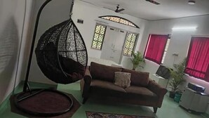 A living room with a hanging chair, a sofa, a radiator, and a window with red curtains. - Blumint 303 (Bengaluru)