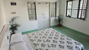 A bedroom with a bed, a door, windows, and a potted plant. - Blumint 303 (Bengaluru)