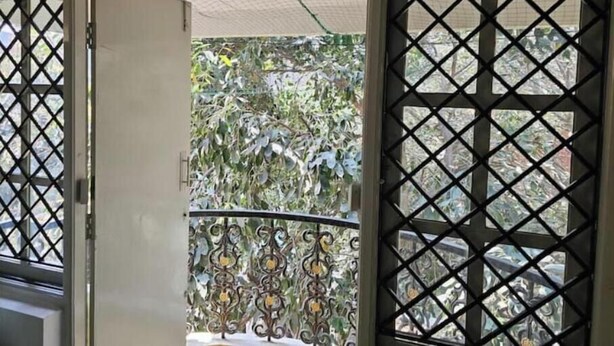 A room with a sliding glass door leading to a balcony with a metal railing and greenery outside.