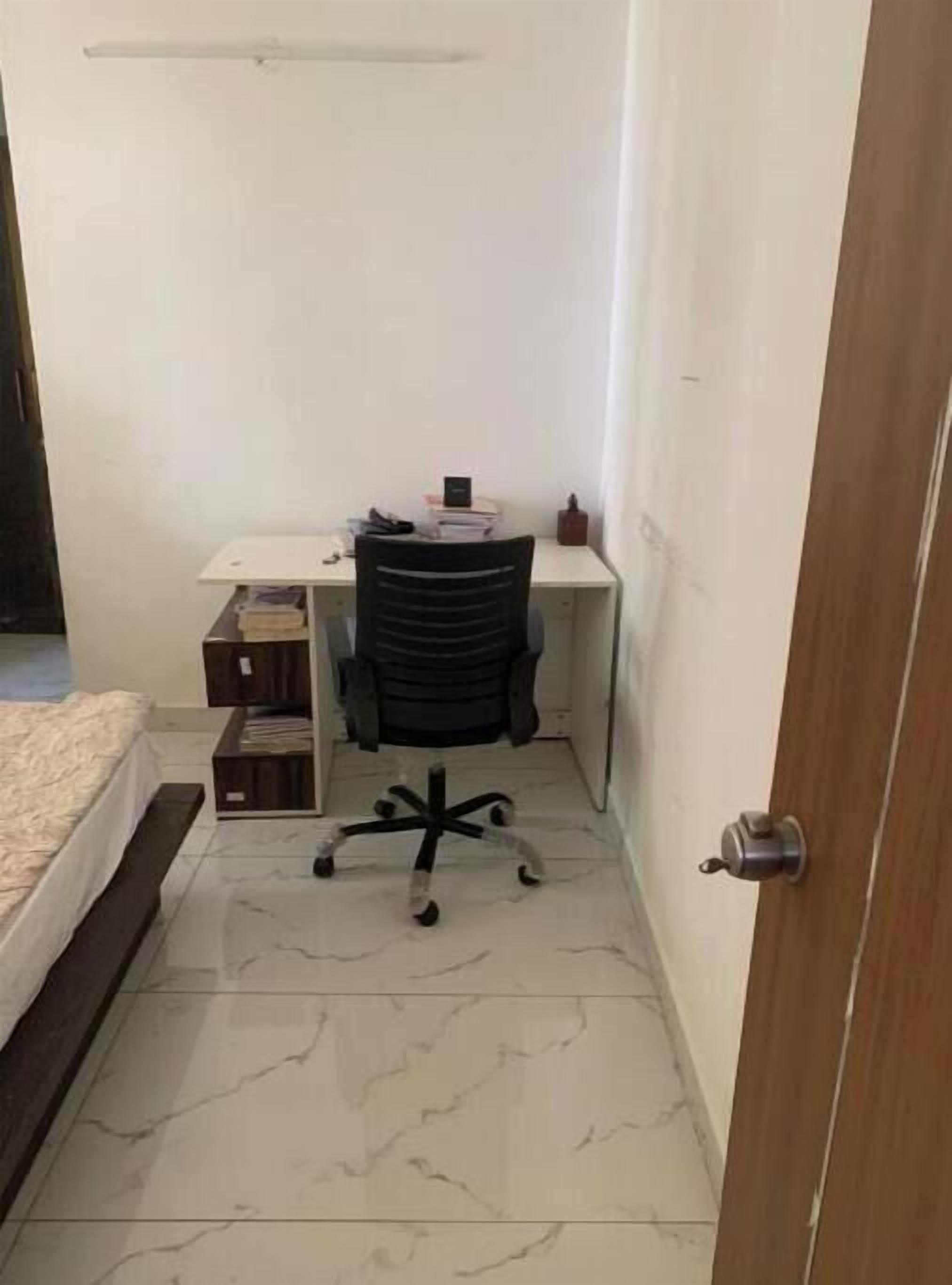 A small, narrow room with a bed, a desk with a chair, and a door.