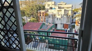 A view from a balcony with a metal railing, overlooking a residential area with multiple buildings, some with red roofs and others with white walls.