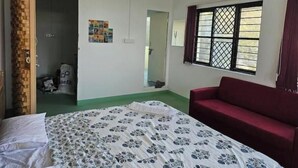A bedroom with a bed, a red sofa, a window with bars, and a door leading to another room.