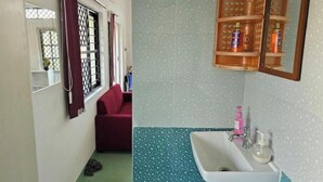 A room with a window, a red sofa, a sink with toiletries, and a wooden cabinet with bottles.