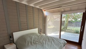 A bedroom with a bed, a nightstand, a lamp, and a large window.