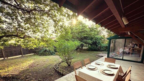 An outdoor patio with a table set for four, surrounded by wooden chairs, under a wooden pergola.